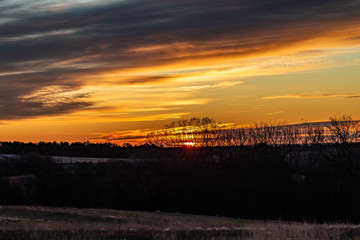 Golden sunrise over a rural countryside with trees in silhouette