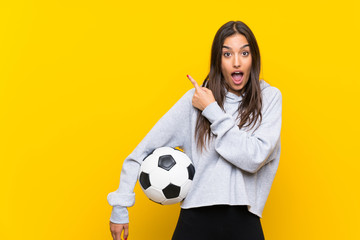 Young football player woman over isolated yellow background surprised and pointing side
