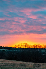 Dramatic autumn sunrise with a treeline silhouette in purple, red, and orange in the clouds