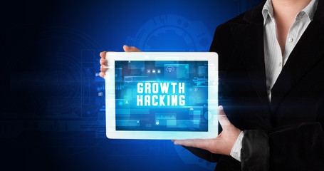 Young business person working on tablet and shows the digital sign: GROWTH HACKING