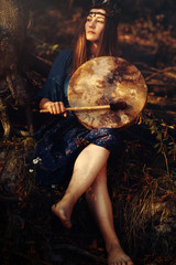 Naklejka premium beautiful shamanic girl playing on shaman frame drum in the nature.