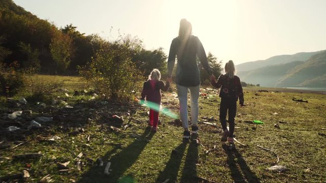 Ecological issue: mother walking with her daughters on land full of garbage