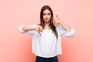 Fototapeta premium Young woman over isolated pink background making good-bad sign. Undecided between yes or not