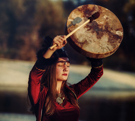 beautiful shamanic girl playing on shaman frame drum in the nature.