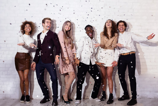 Positive Young People Standing Under Falling Confetti Having Fun Indoor