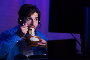 Male gamer eating noodle soup, playing video games © Prostock-studio