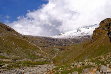 Fototapeta premium A beautiful picture of the Himalayan mountains with snowy peaks and green grass slopes on which horses graze in the distance. The stones formed a dry rocky stream of brown-gray color.