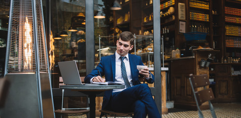 Young businessman with coffee cup writing on notebook