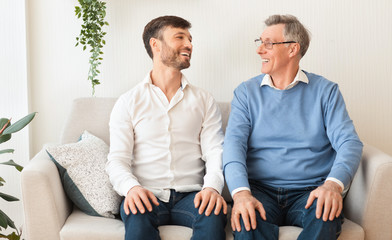 Elderly Father And Mature Son Smiling Sitting On Couch At Home