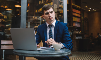 Serious young businessman working on laptop and frowning while thinking