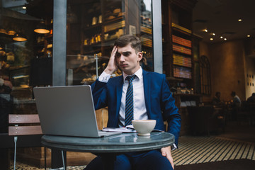 Displeased young businessman looking at laptop and holding head