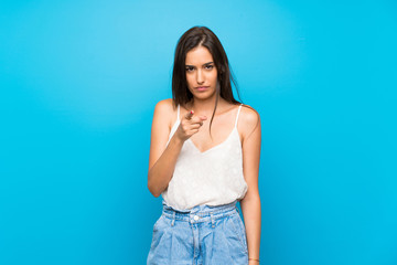 Young woman over isolated blue background frustrated and pointing to the front