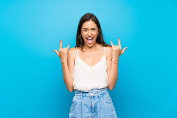 Young woman over isolated blue background making rock gesture