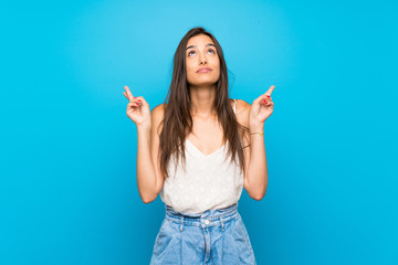 Young woman over isolated blue background with fingers crossing and wishing the best