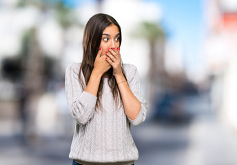 Fototapeta premium Young hispanic brunette woman covering mouth and looking to the side at outdoors