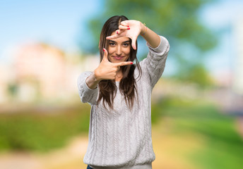 Young hispanic brunette woman focusing face. Framing symbol at outdoors