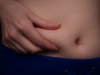 Female belly with excess fat close up. A starting to gain weight young caucasian woman squeezes fat on her waist with her right hand. Unsportsmanlike female body.