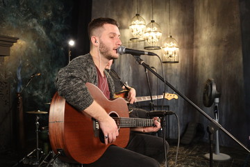 Saint Petersburg, Russia - 23 october  2019: Handsome young man playing acoustic guitar and singing, concert photo, for music and entertainment themes. Dima Iarmolenko musician, vocal guitar