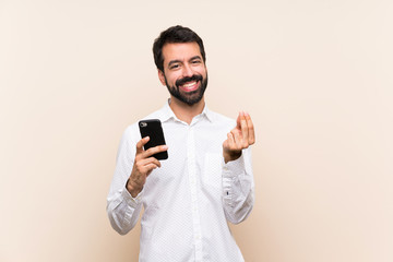 Young man with beard holding a mobile making money gesture