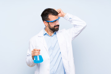 Young scientific holding laboratory flask over isolated background having doubts while scratching head