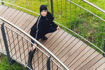 Hijab girl exercising on walkway bridge in early morning. Muslim woman wearing sports clothes doing stretching workout outdoors.