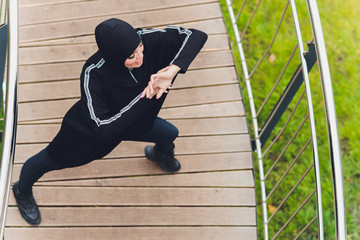 Hijab girl exercising on walkway bridge in early morning. Muslim woman wearing sports clothes doing stretching workout outdoors.