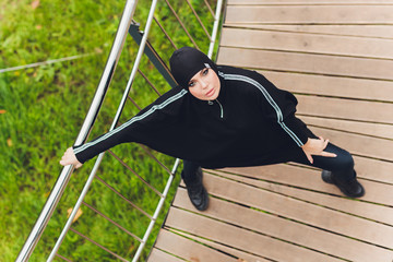 Hijab girl exercising on walkway bridge in early morning. Muslim woman wearing sports clothes doing stretching workout outdoors.