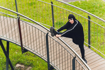 Hijab girl exercising on walkway bridge in early morning. Muslim woman wearing sports clothes doing stretching workout outdoors.
