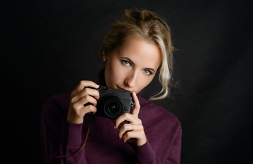 Young pretty woman holding camera over dark background.