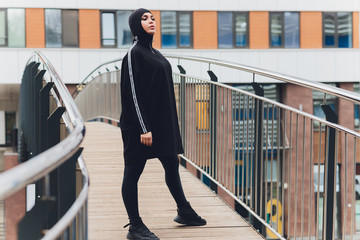 Hijab girl exercising on walkway bridge in early morning. Muslim woman wearing sports clothes doing stretching workout outdoors.