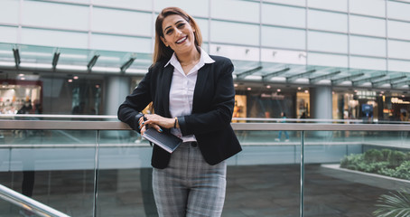 Positive executive leaning on glass fence and looking at camera