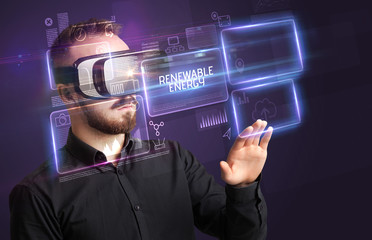 Businessman looking through Virtual Reality glasses with RENEWABLE ENERGY inscription, new technology concept