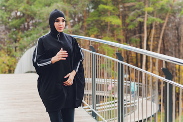 Hijab girl exercising on walkway bridge in early morning. Muslim woman wearing sports clothes doing stretching workout outdoors.