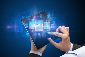 Businessman holding a foldable smartphone with GAMING inscription, new technology concept