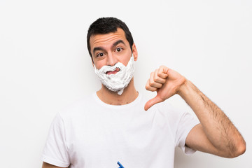 Man shaving his beard over isolated white background showing thumb down