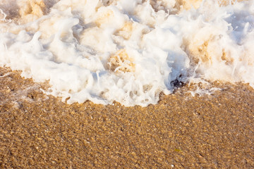 sea waves splash foam on the sunny beach.  mess of salt water and sand in evening light. dynamic nature texture