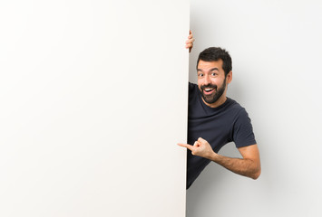 Young handsome man with beard holding a big empty placard and pointing it