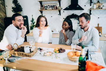 Cheerful group of friends eating and drinking in kitchen enjoying New Year weekend at home