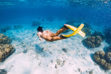 Free diver young girl with yellow fins glides over sandy bottom and corals.