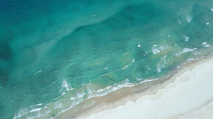 White sand by the sea with blue water and foamy waves.