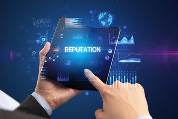 Businessman holding a foldable smartphone with REPUTATION inscription, successful business concept