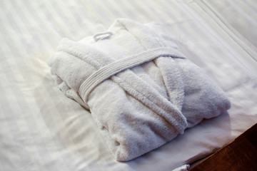 Clean folded bathrobe on white bed.