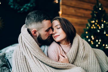 Coup[le embracing rolled in rug with Christmas tree on background