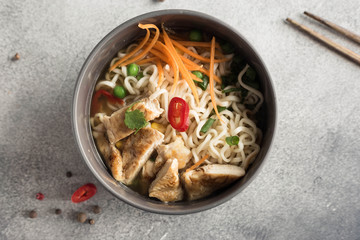 Spicy Asian noodles with chicken in a gray ceramic round plate on a gray background. Top view image