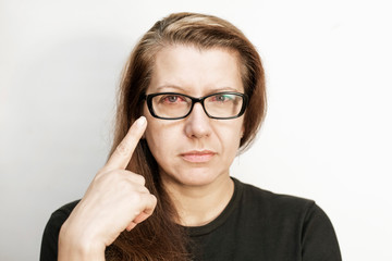 Middle-aged woman with glasses pointing finger at her red, sick eye, sad woman because she has...