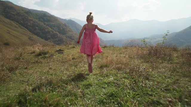 Attractive little blond girl running straight to a mountain valley