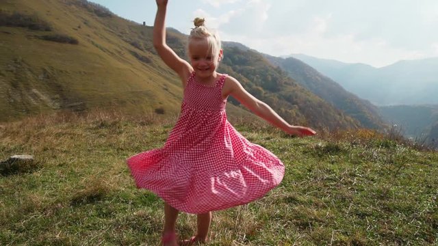 Attractive little blond girl spinning in front of mountain valley
