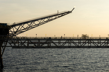 Silhouette of an oil production platform connected with a bridge at oil field during sunset