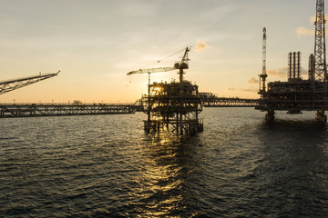 Fototapeta na wymiar Silhouette of an oil production platform connected with a bridge at oil field during sunset