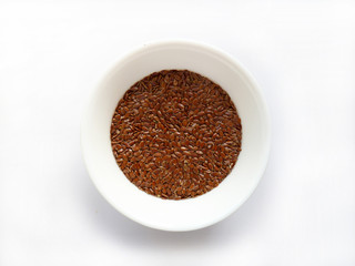 Flax seeds or linseed in white bowl isolated on white background. Bio organic raw flax seeds in ceramic bowl, top view. Bowl of dried flax seeds on white.